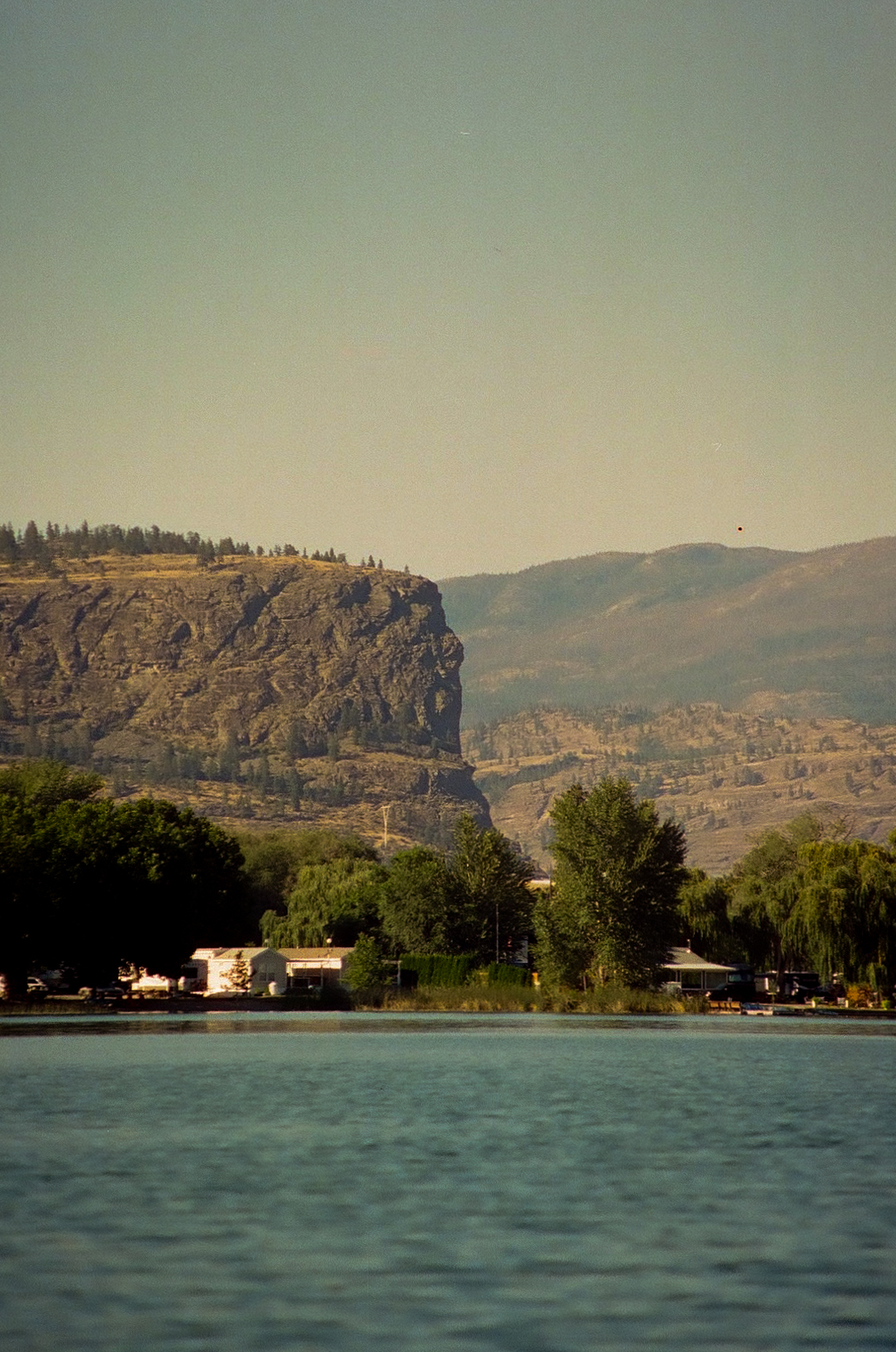 A calm lake below a steep rocky bluff and dry hills.
