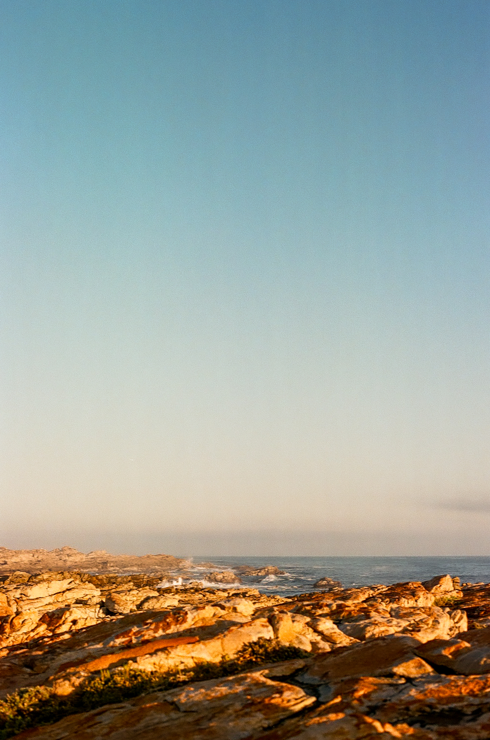 Rocky shoreline lit gold at sunset, sea and open sky beyond.